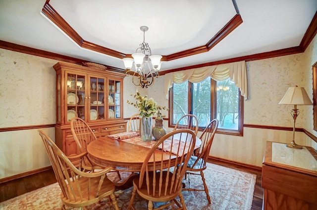 dining space with a raised ceiling, wood-type flooring, ornamental molding, and an inviting chandelier