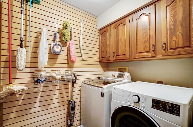 clothes washing area with washer and clothes dryer, cabinets, and wooden walls