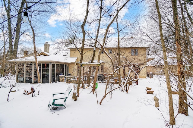 snow covered rear of property with a sunroom