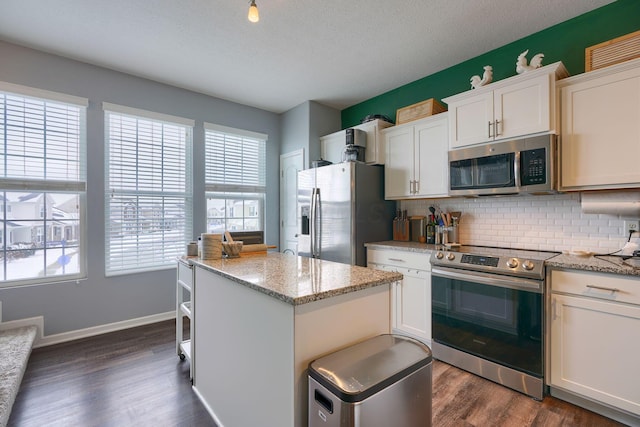 kitchen with white cabinets, dark hardwood / wood-style floors, light stone counters, and appliances with stainless steel finishes