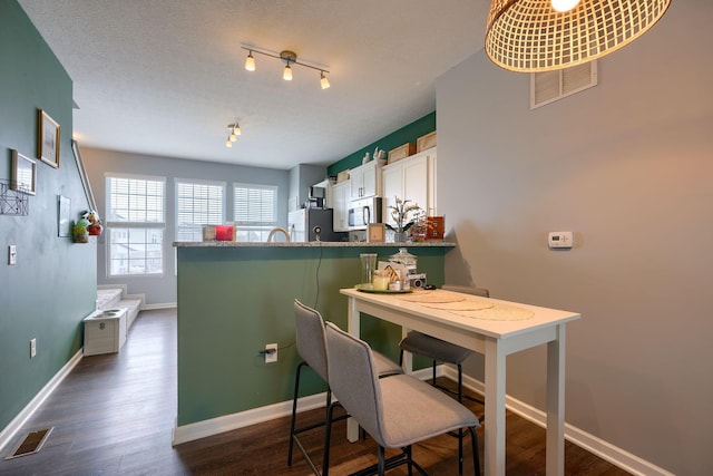 kitchen featuring stainless steel refrigerator, kitchen peninsula, white cabinetry, and a kitchen breakfast bar