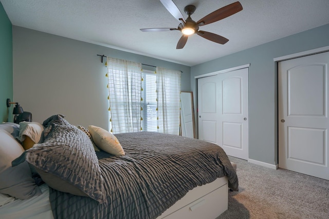 bedroom with carpet flooring, a textured ceiling, ceiling fan, and multiple closets