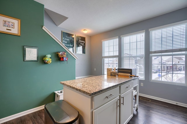 kitchen featuring dark hardwood / wood-style flooring, light stone countertops, plenty of natural light, and white cabinets