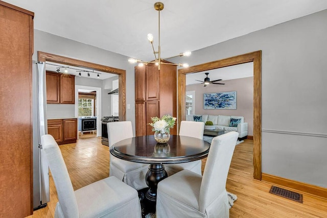 dining space with ceiling fan with notable chandelier and light hardwood / wood-style flooring