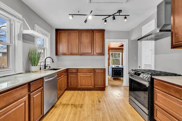 kitchen with sink, wall chimney exhaust hood, stainless steel appliances, light hardwood / wood-style flooring, and track lighting