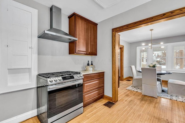 kitchen featuring wall chimney exhaust hood, hanging light fixtures, stainless steel gas range, a notable chandelier, and light hardwood / wood-style floors