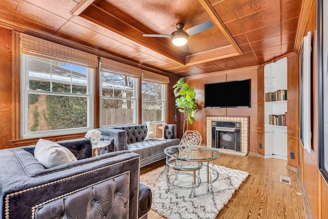 living room featuring wood walls, ceiling fan, light hardwood / wood-style floors, wood ceiling, and a tiled fireplace