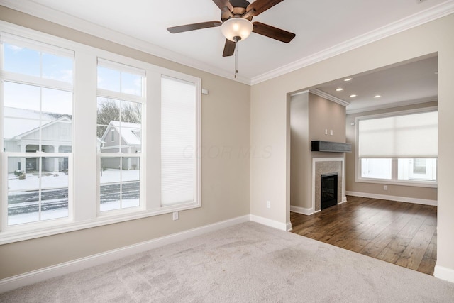 unfurnished living room featuring baseboards, a ceiling fan, a glass covered fireplace, ornamental molding, and dark colored carpet