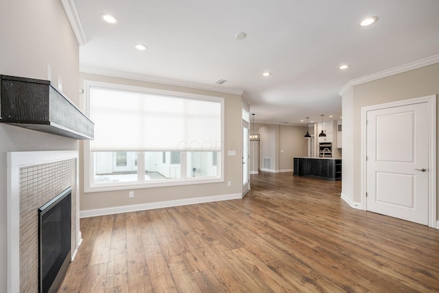 unfurnished living room featuring recessed lighting, a tiled fireplace, wood finished floors, and crown molding