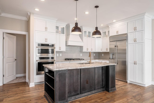 kitchen featuring an island with sink, glass insert cabinets, light stone countertops, stainless steel appliances, and open shelves