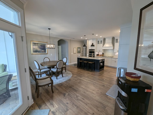 dining space featuring arched walkways, ornamental molding, dark wood finished floors, and a chandelier