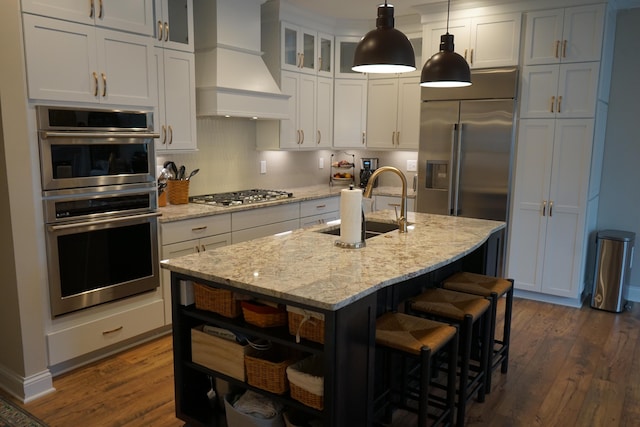 kitchen featuring stainless steel appliances, premium range hood, a sink, glass insert cabinets, and pendant lighting