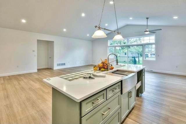 kitchen with ceiling fan, light stone counters, light hardwood / wood-style flooring, vaulted ceiling, and a kitchen island with sink