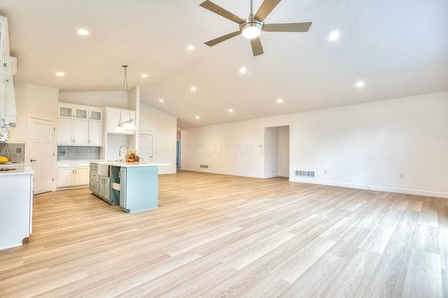 kitchen with light hardwood / wood-style flooring, backsplash, an island with sink, decorative light fixtures, and white cabinets