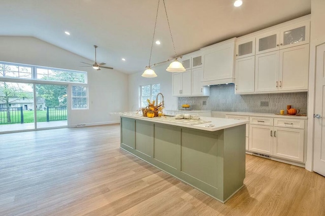 kitchen with vaulted ceiling, decorative light fixtures, white cabinetry, and a kitchen island with sink