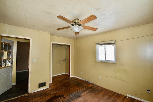 unfurnished bedroom with a textured ceiling, ceiling fan, dark wood-type flooring, and a closet