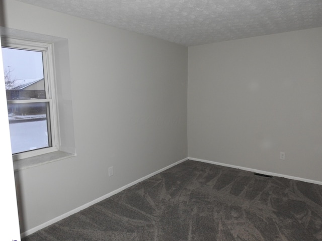 empty room with a textured ceiling and dark carpet