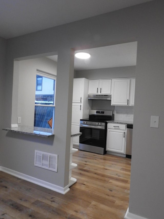 kitchen with backsplash, light stone counters, stainless steel appliances, wood-type flooring, and white cabinets