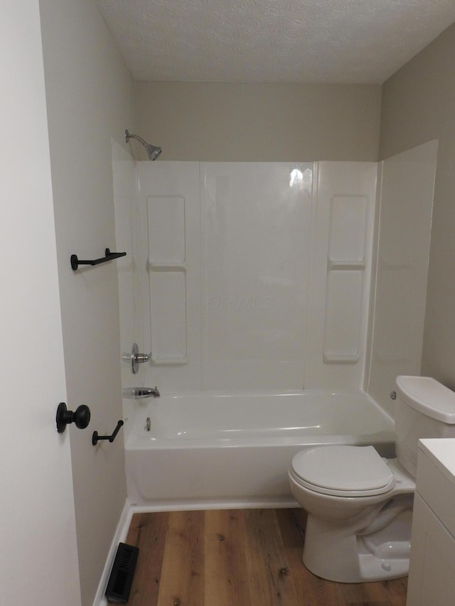 full bathroom with wood-type flooring, a textured ceiling, toilet, and shower / washtub combination