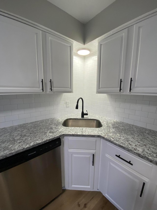 kitchen featuring white cabinets, sink, stainless steel dishwasher, light stone countertops, and wood-type flooring