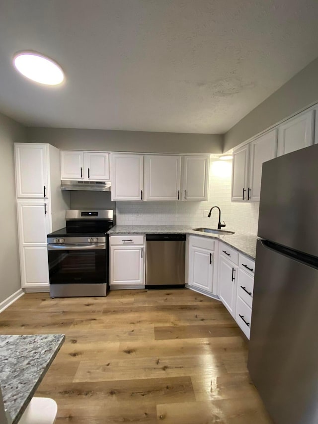 kitchen with sink, light stone countertops, light wood-type flooring, appliances with stainless steel finishes, and white cabinetry