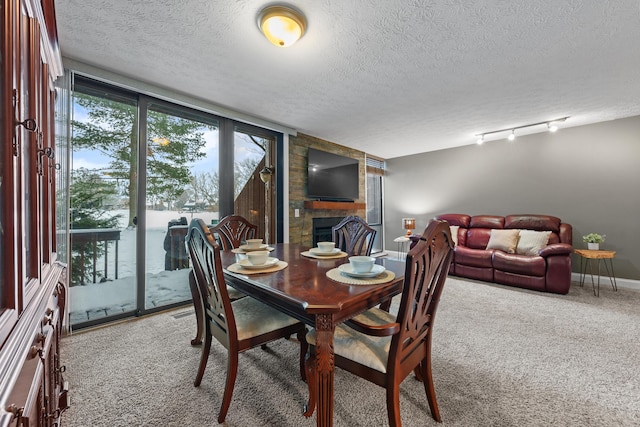 carpeted dining space featuring rail lighting, a textured ceiling, a large fireplace, and floor to ceiling windows