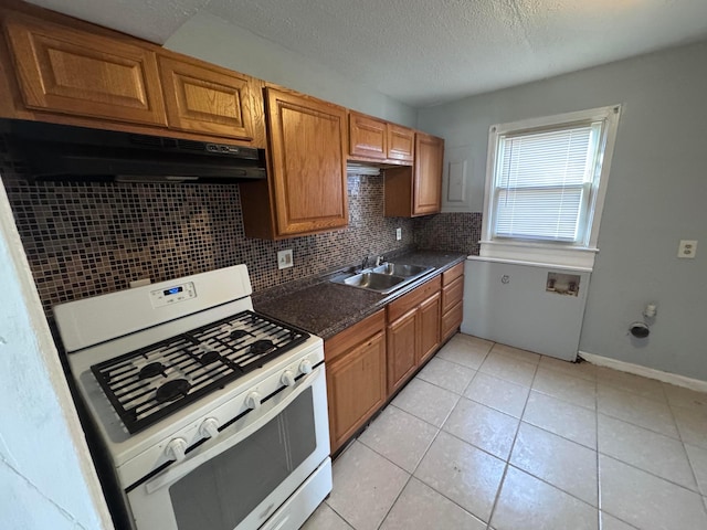 kitchen with white gas range, sink, backsplash, a textured ceiling, and light tile patterned flooring