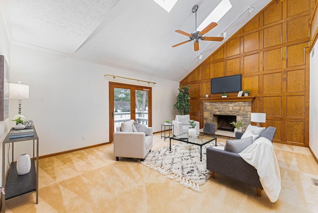 carpeted living room featuring a skylight, a textured ceiling, ceiling fan, high vaulted ceiling, and a stone fireplace