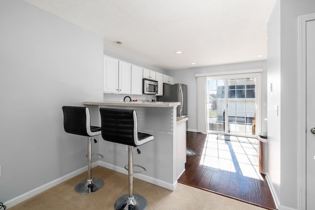 kitchen with white cabinets, dark hardwood / wood-style flooring, a kitchen bar, kitchen peninsula, and stainless steel appliances