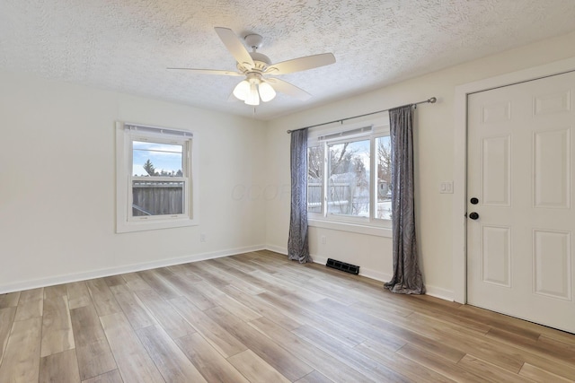 unfurnished room featuring a textured ceiling, light hardwood / wood-style flooring, ceiling fan, and a healthy amount of sunlight