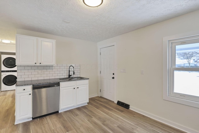 kitchen with tasteful backsplash, sink, stacked washer and clothes dryer, dishwasher, and white cabinetry