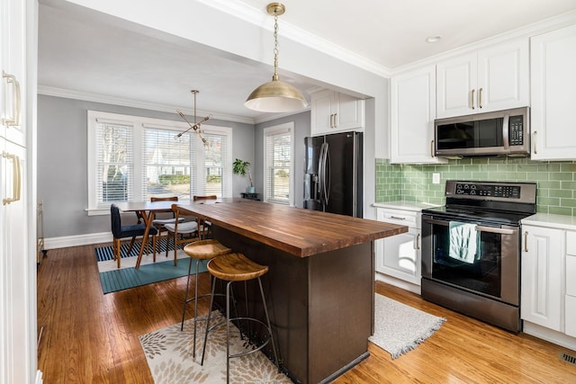 kitchen with pendant lighting, butcher block countertops, crown molding, appliances with stainless steel finishes, and white cabinetry