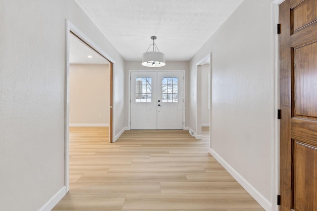 foyer entrance featuring light wood-type flooring, a textured ceiling, and french doors