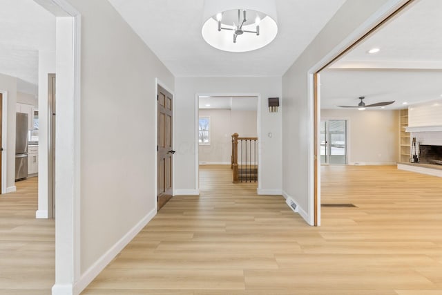 hallway featuring built in shelves, light wood-type flooring, and a notable chandelier