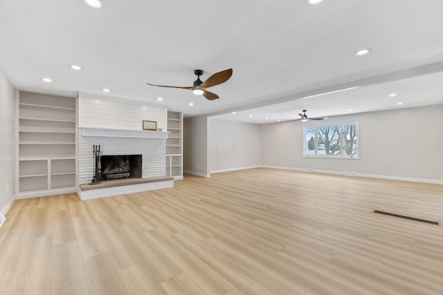 unfurnished living room with ceiling fan, light wood-type flooring, built in shelves, and a brick fireplace