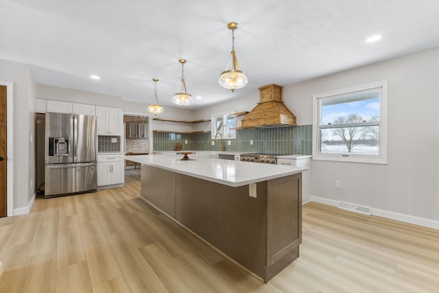 kitchen with backsplash, white cabinets, hanging light fixtures, and stainless steel refrigerator with ice dispenser