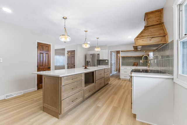 kitchen featuring a center island, stainless steel refrigerator with ice dispenser, decorative backsplash, decorative light fixtures, and custom range hood