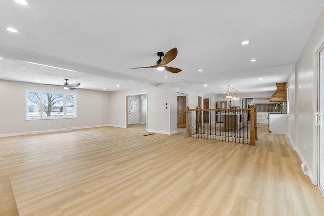 unfurnished living room with ceiling fan with notable chandelier, light wood-type flooring, and sink