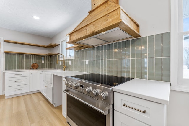 kitchen with white cabinetry, stainless steel range, light hardwood / wood-style flooring, backsplash, and custom range hood