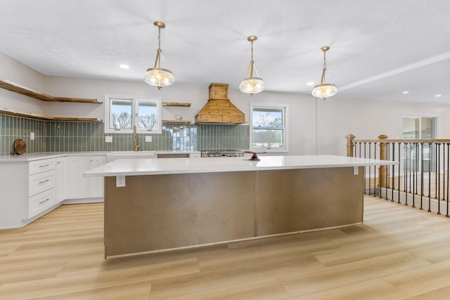 kitchen with white cabinets, custom range hood, tasteful backsplash, and hanging light fixtures