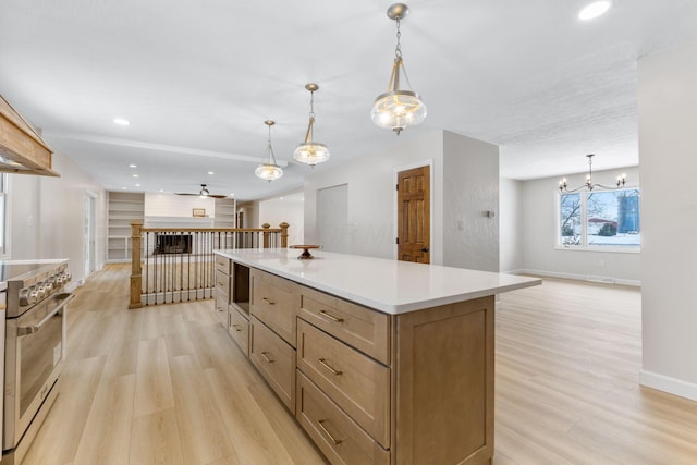 kitchen with a center island, pendant lighting, light hardwood / wood-style floors, stainless steel stove, and ceiling fan with notable chandelier