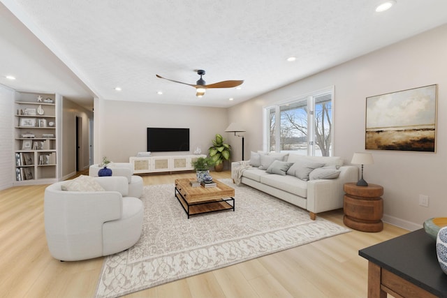 living room with built in shelves, ceiling fan, hardwood / wood-style floors, and a textured ceiling