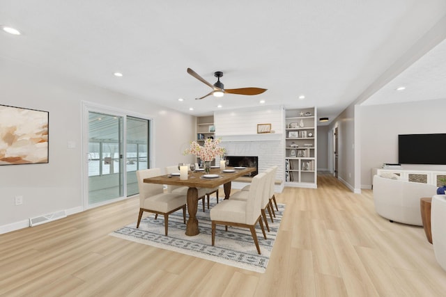 dining area with a fireplace, light wood-type flooring, built in features, and ceiling fan