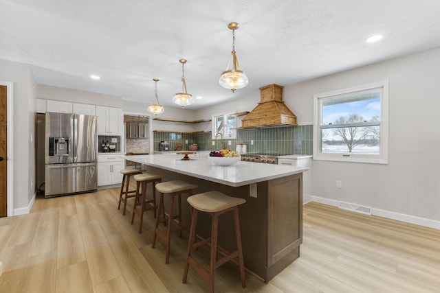 kitchen with pendant lighting, custom exhaust hood, white cabinets, decorative backsplash, and stainless steel fridge