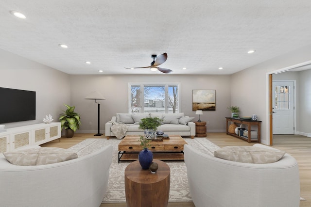 living room featuring ceiling fan, light hardwood / wood-style flooring, and a textured ceiling