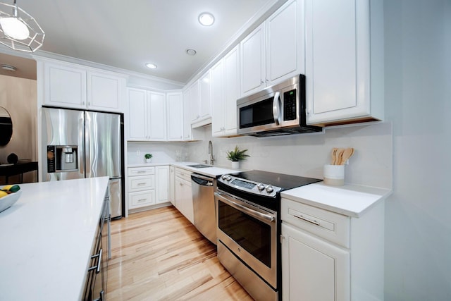 kitchen with white cabinetry, sink, stainless steel appliances, pendant lighting, and light hardwood / wood-style floors