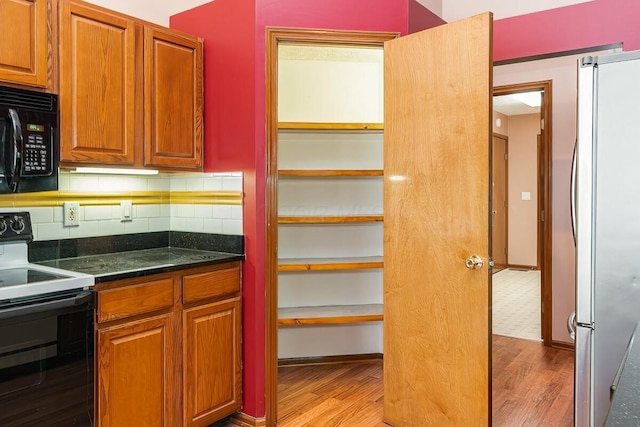 kitchen with electric range, stainless steel fridge, backsplash, and light hardwood / wood-style flooring