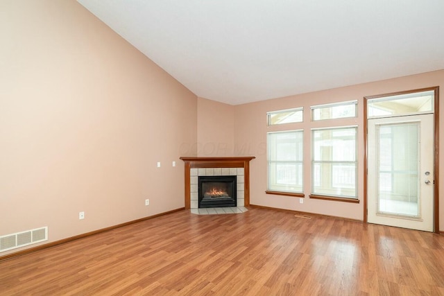 unfurnished living room with a tile fireplace, light hardwood / wood-style floors, and vaulted ceiling