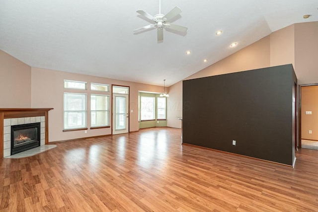 unfurnished living room featuring ceiling fan, light hardwood / wood-style floors, high vaulted ceiling, and a tiled fireplace