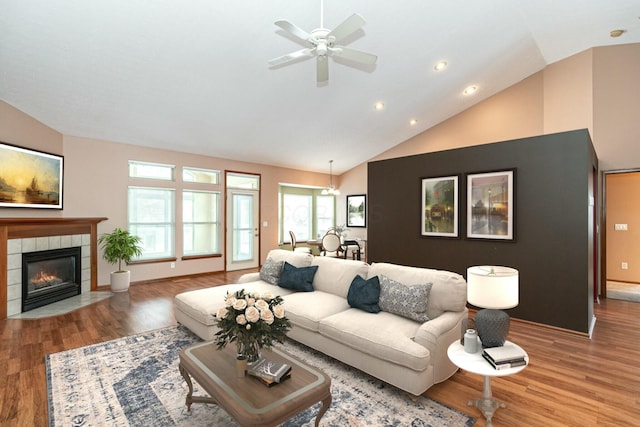 living room featuring hardwood / wood-style flooring, ceiling fan, lofted ceiling, and a tiled fireplace